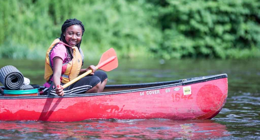 A person wearing a life jacket smiles while holding a paddle in a red canoe